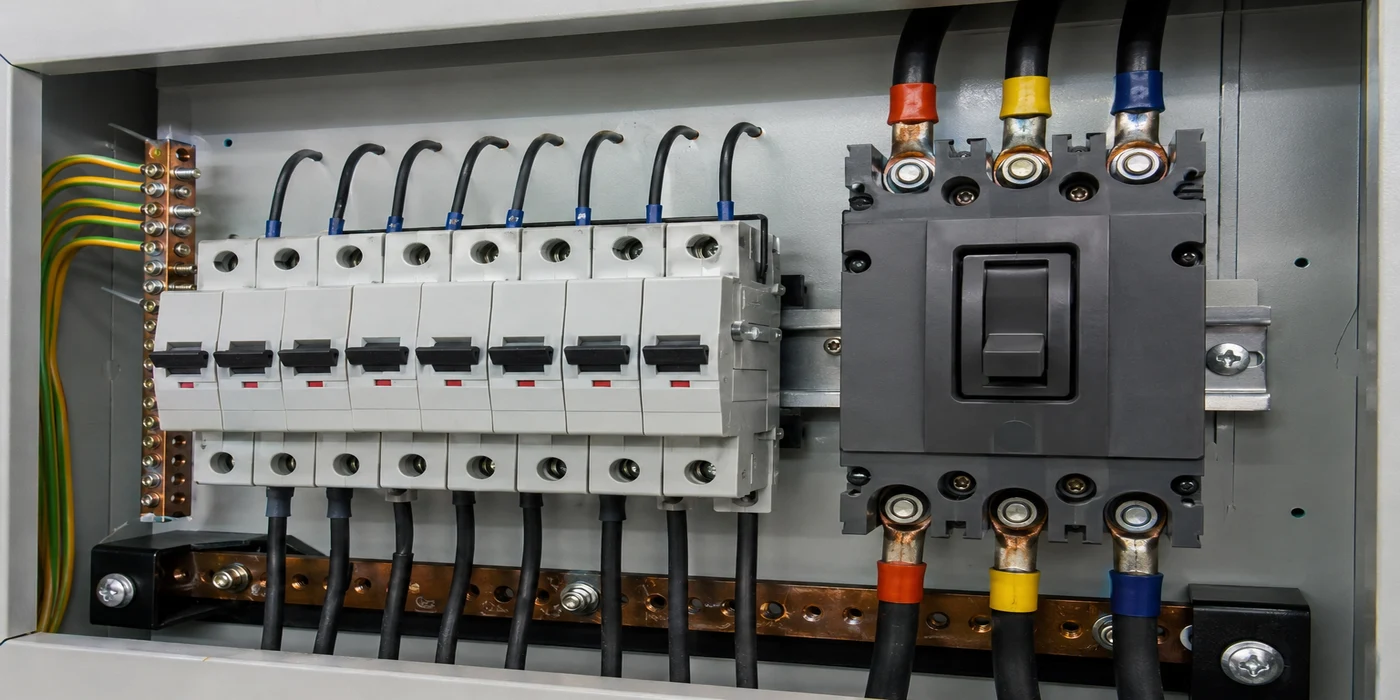 Open electrical panel showing a row of miniature circuit breakers next to a larger molded case circuit breaker for size comparison