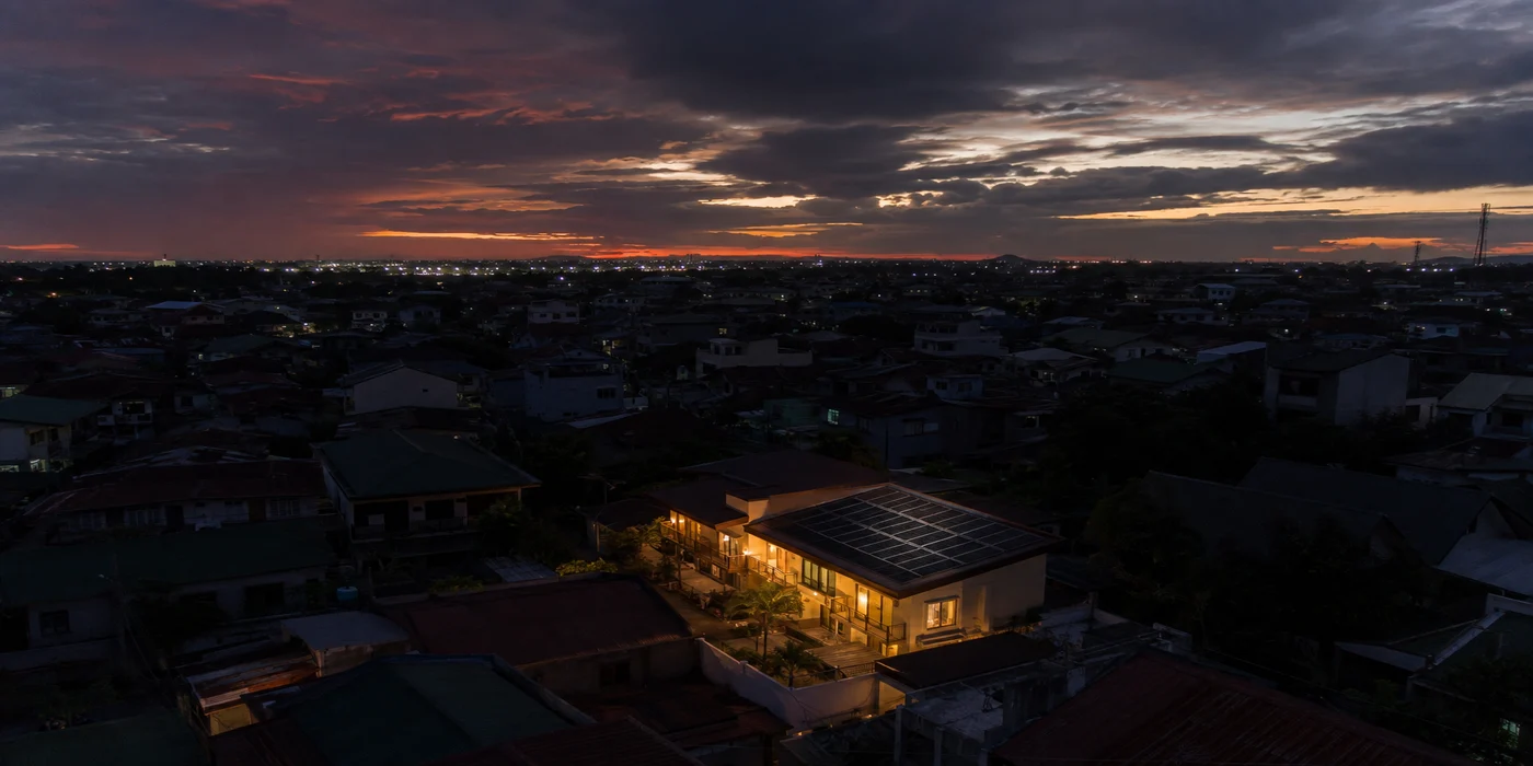 One house glowing with lights on during a neighborhood brownout, powered by rooftop solar and battery backup