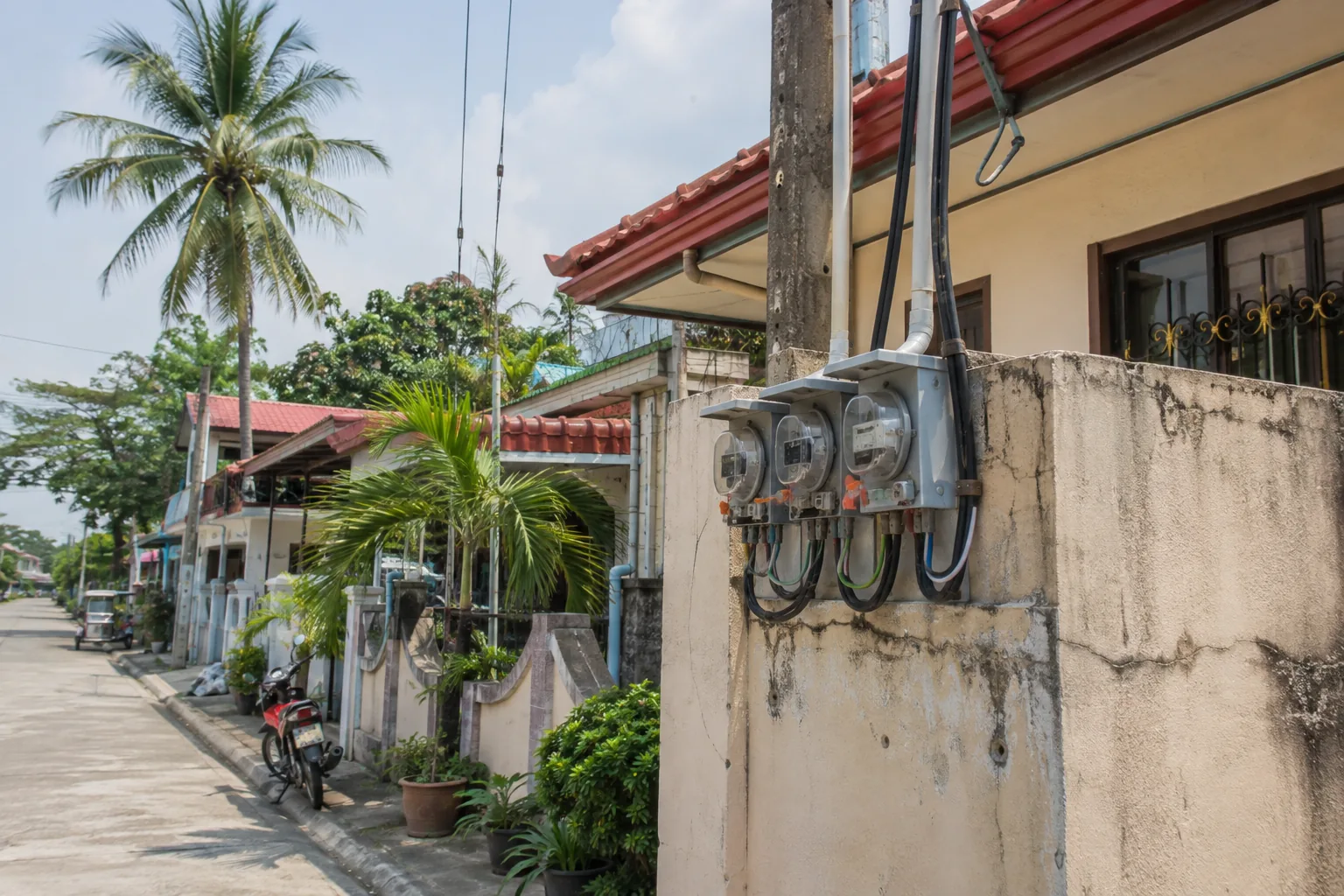 Three electric meters mounted on a shared concrete wall between neighboring homes in a subdivision in the Philippines
